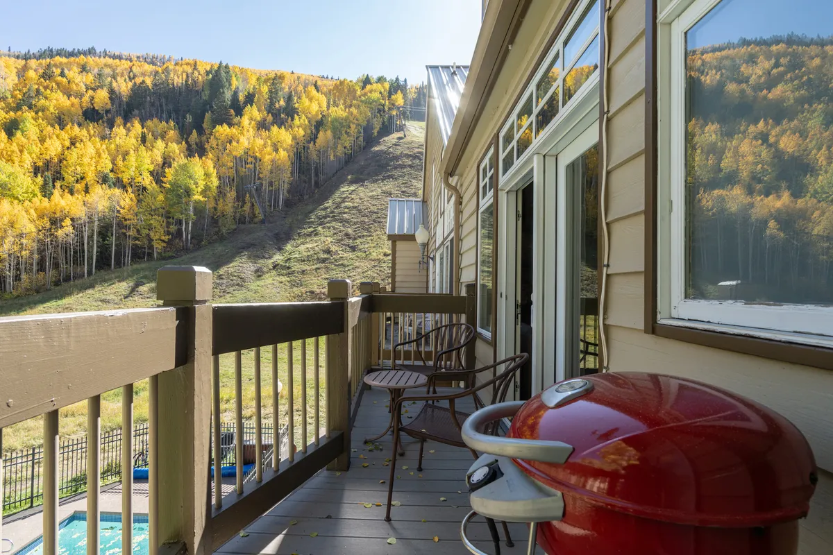 An exterior shot of a balcony featuring a grill, surrounded by vibrant autumn foliage and overlooking a mountain slope. The scene is cheerful and relaxed, highlighting the enjoyment of outdoor cooking, socializing, and soaking in natural beauty—key aspects of al fresco dining and communal barbecue spaces.