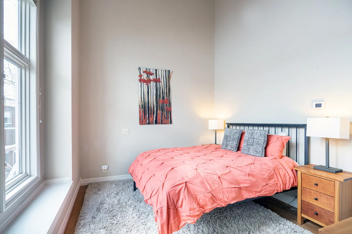 A cozy bedroom featuring a bed with coral bedding, warm lighting from bedside lamps, and inviting artwork. The room radiates comfort and provides an intimate, restful atmosphere perfect for family or guests.