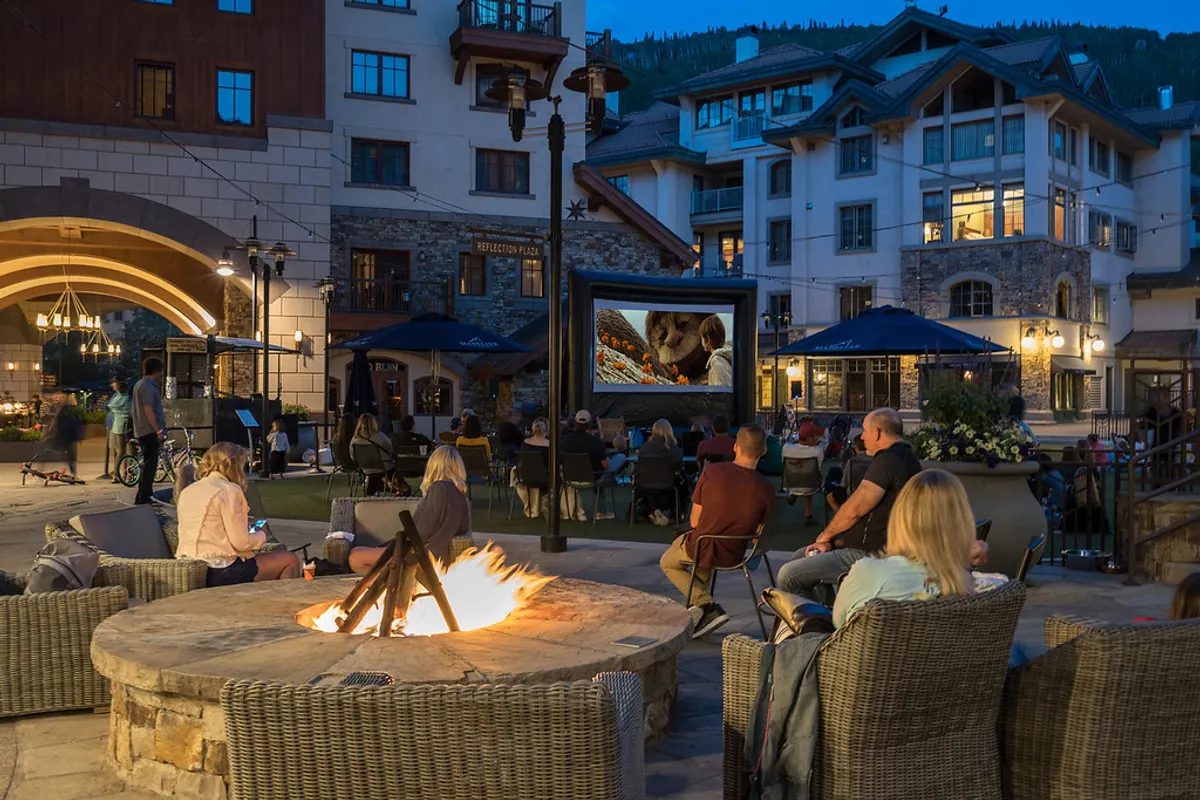 A cozy outdoor communal space featuring a fire pit, ample seating, and an outdoor movie screen. Surrounded by mountain air, this setting invites relaxation and socializing under the stars—an ideal complement to spa-like experiences and après-ski gatherings.
