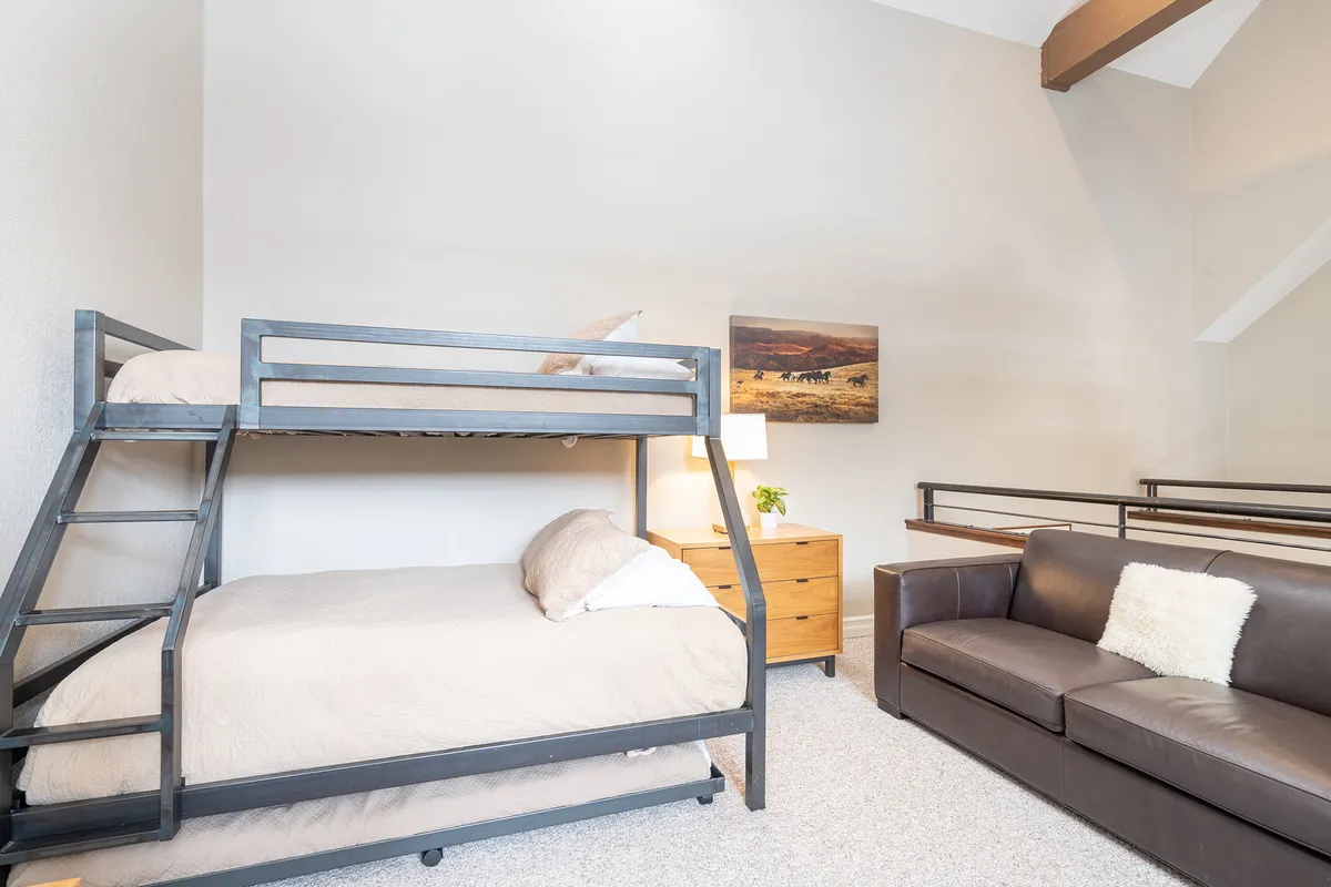 A family-friendly loft area with bunk beds, a comfy sofa, chest of drawers, and playful wall art. The space feels welcoming and communal, ideal for children or groups sharing stories above the main living area.