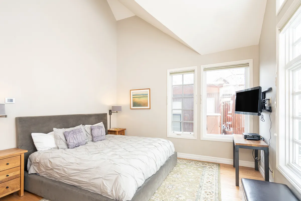 A serene bedroom with a large bed positioned near bright windows, complemented by tasteful artwork. Natural light streams in, creating a peaceful setting ideal for rest and relaxation, with the view providing a strong sense of place and comfort.