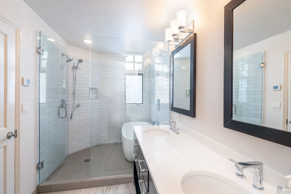 A contemporary bathroom with a glass shower enclosure, luxurious freestanding bathtub, and double vanity with mirrors. The space exudes modern elegance and offers a spa-like retreat for relaxation.