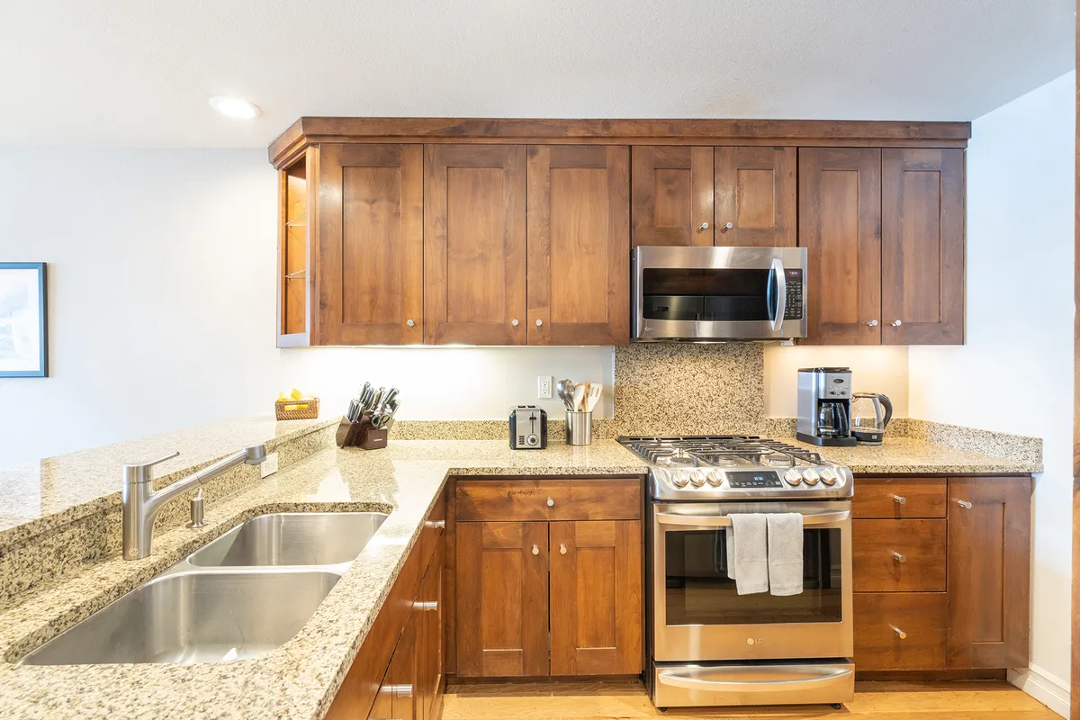 This image showcases a warm and homey kitchen featuring granite countertops, rich wood cabinetry, and sleek stainless steel appliances. The spacious layout is designed for cooking and entertaining, with multiple surfaces for meal prep and gathering.