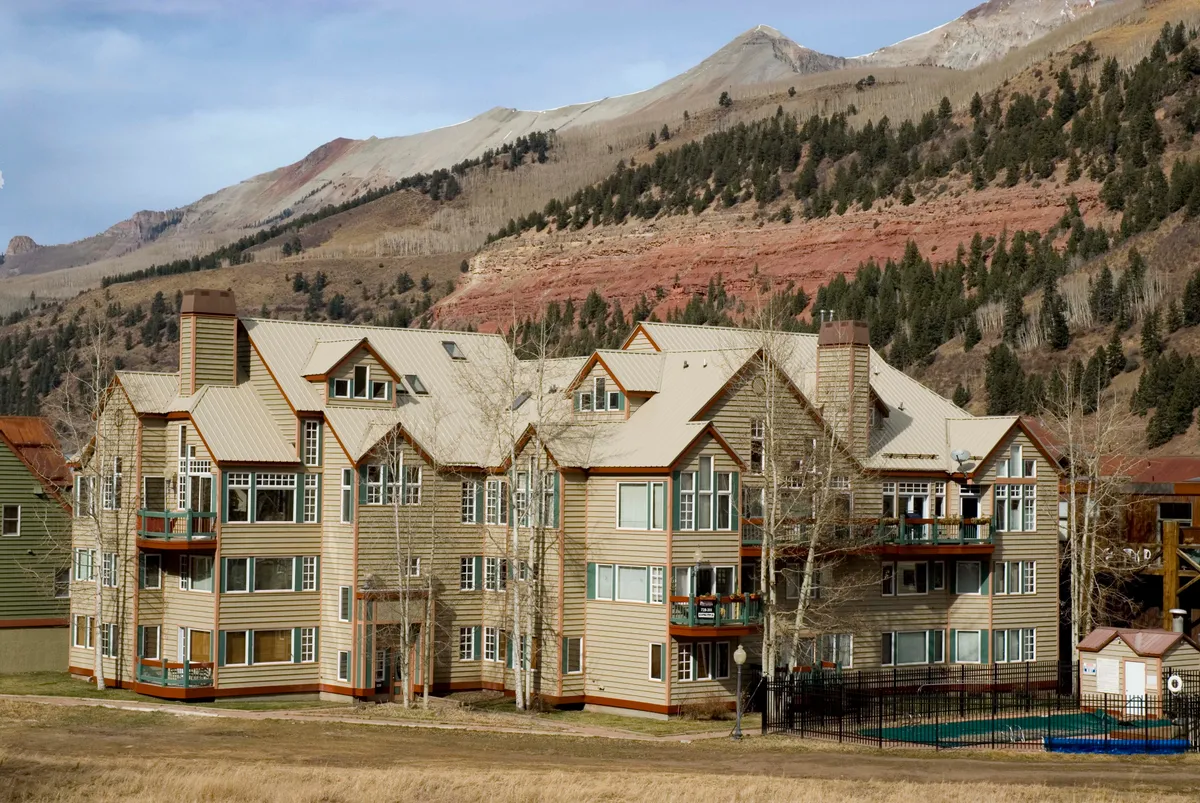 This image shows the multi-level Etta Place building with the surrounding mountains in the background. The swimming pool area is visible, creating a welcoming and spacious outdoor environment perfect for family relaxation and gatherings. The soft evening light hints at sunset views from the balconies, and there are barbecue and picnic areas in the yard, reinforcing a communal and family-oriented atmosphere.